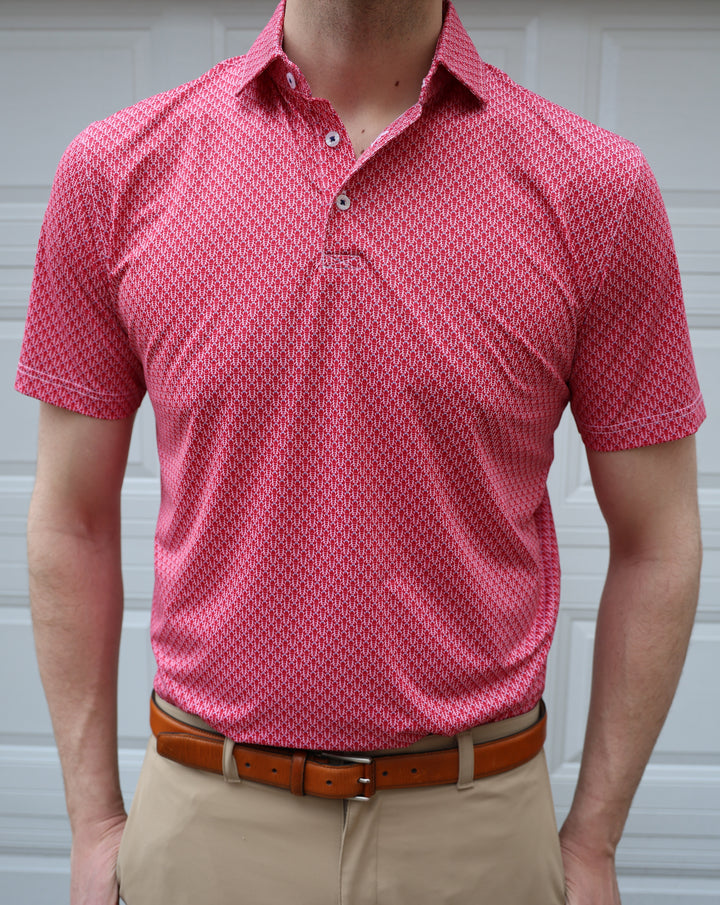 A person is wearing a short-sleeved, red patterned polo shirt paired with beige pants and a brown belt, standing against a neutral background.