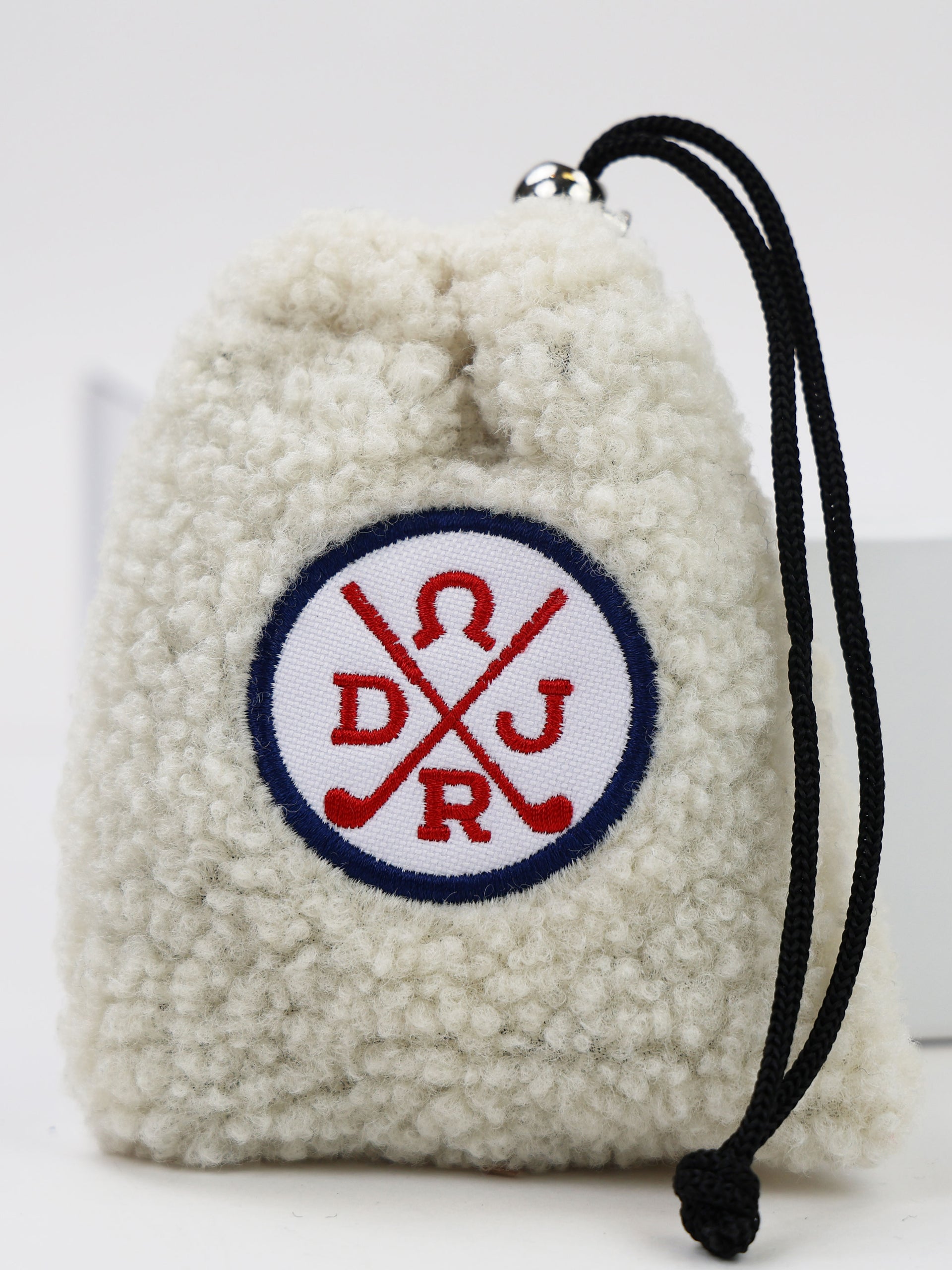 Cream-colored sherpa pouch with navy and red crossed golf clubs emblem and black drawstring cord.