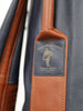 Close-up of a MacKenzie Walker golf bag label featuring a navy leather patch with gold embossing attached to a cognac and charcoal leather strap.