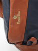 Cognac leather messenger bag with Donald Ross embroidered branding and decorative floral crest detail, displayed with navy blue leather panels visible on either side.