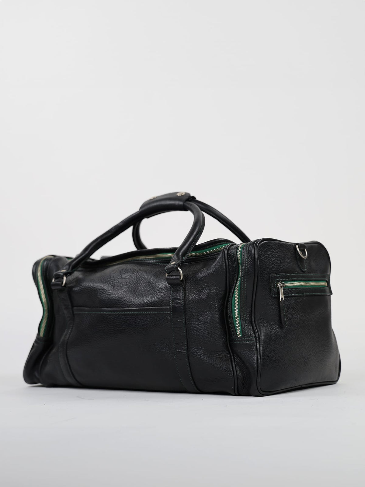 Black leather travel bag with green zippers, featuring two sturdy handles and front pocket, placed on a white background