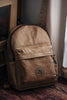 A handcrafted tan leather backpack with a pebble grain finish featuring adjustable shoulder straps and a top carry handle.