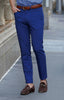 Man wearing royal blue chinos with a cognac leather belt and brown suede loafers stands on a city street.