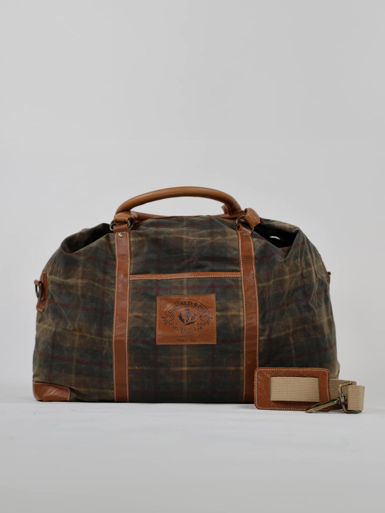 Vintage-style duffel bag with a plaid pattern, brown leather accents, sturdy handles, and a prominent leather patch, set against a plain background