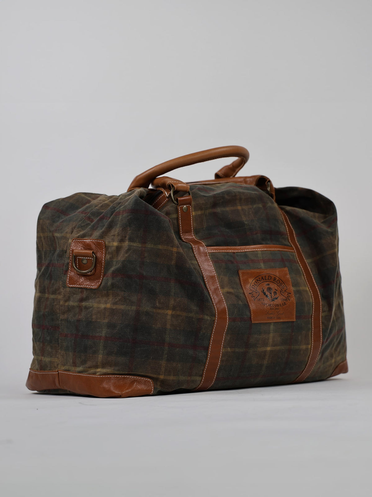 A stylish, plaid-patterned duffel bag with brown leather accents and handles against a plain background