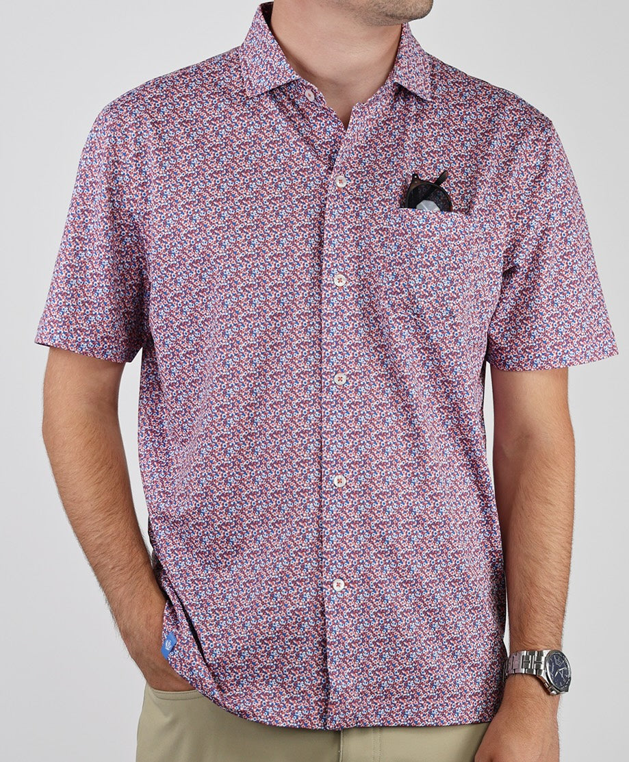 Man wearing a short-sleeve button-up shirt in a red and blue floral print pattern with a black pocket detail.