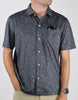 Man wearing a charcoal short-sleeve button-up shirt with a repeating stick figure pattern and a chest pocket.