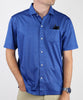 Man wearing a royal blue short-sleeve polo shirt with all-over geometric pattern and white button closure, styled with a black pocket square and khaki trousers.
