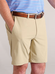 A person wearing tan shorts with hands in pockets is shown from the waist down. They wear a brown textured belt and a blue-striped shirt.