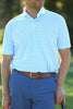 A man wearing a light blue striped polo shirt and blue pants stands while holding a golf club.