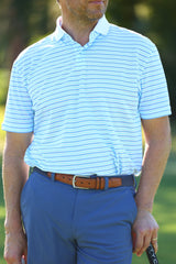 A man wearing a light blue striped polo shirt and blue pants stands while holding a golf club.