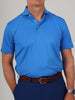 A man wearing a bright blue polo shirt is shown from the chest down. He has a brown leather belt and a silver watch. The background is plain gray.