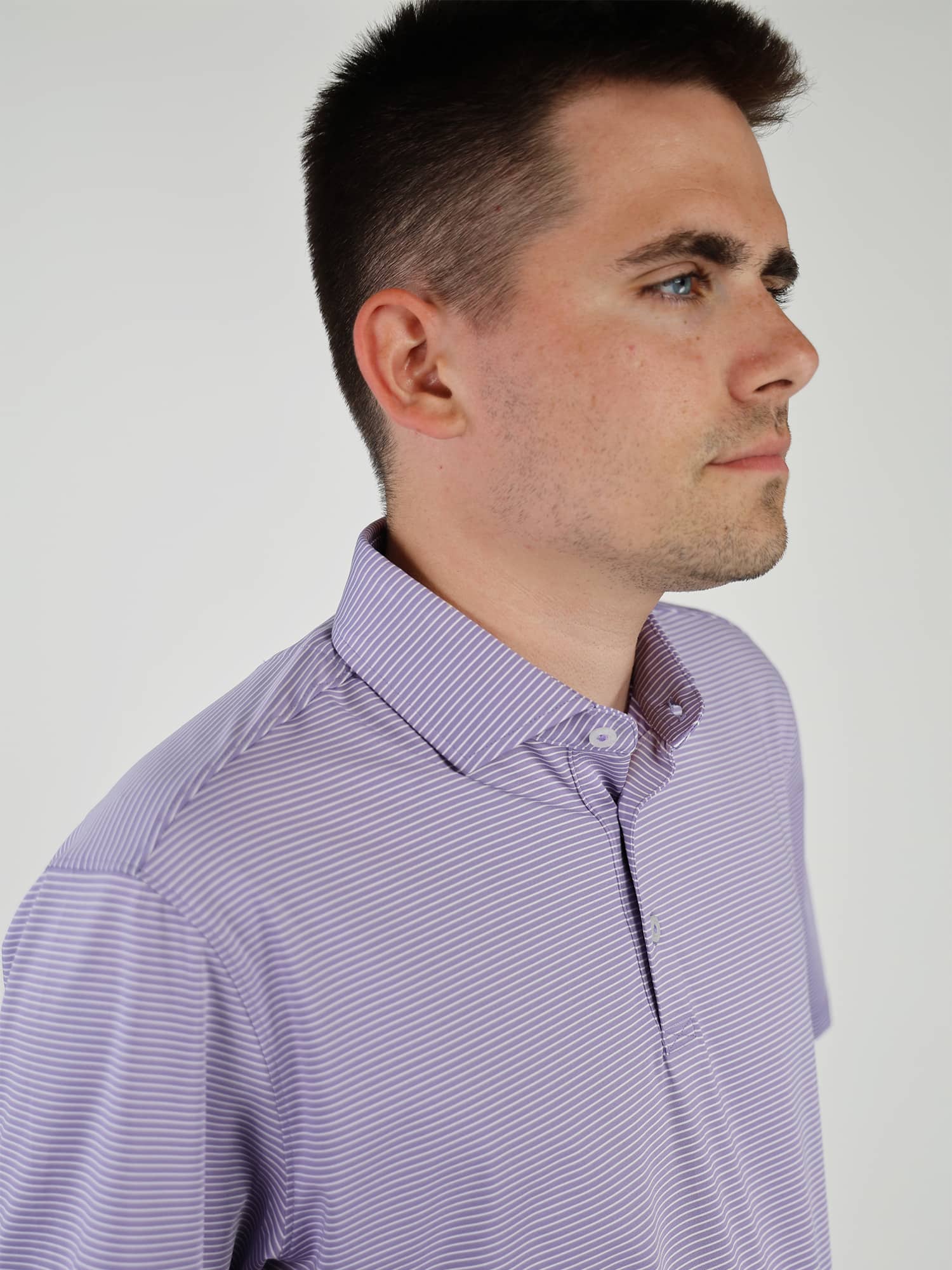 A person in a light purple striped polo shirt looks to the right. The background is plain white, and the expression is calm and neutral
