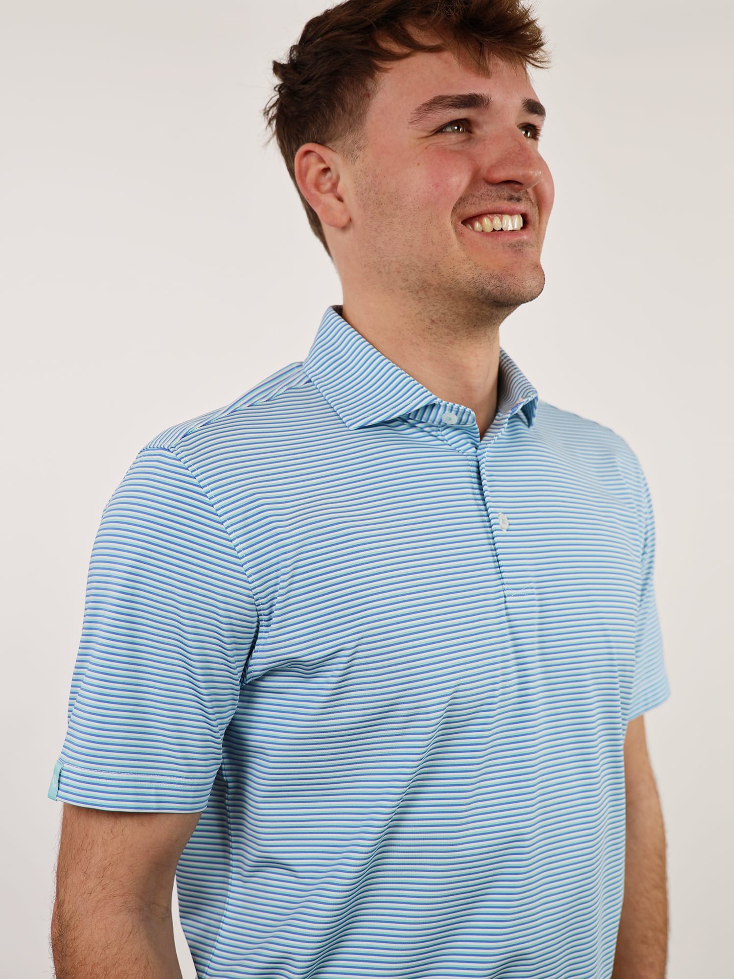 Smiling man in blue striped polo shirt, looking upward with joy. Neutral background enhances focus on his cheerful expression and casual attire