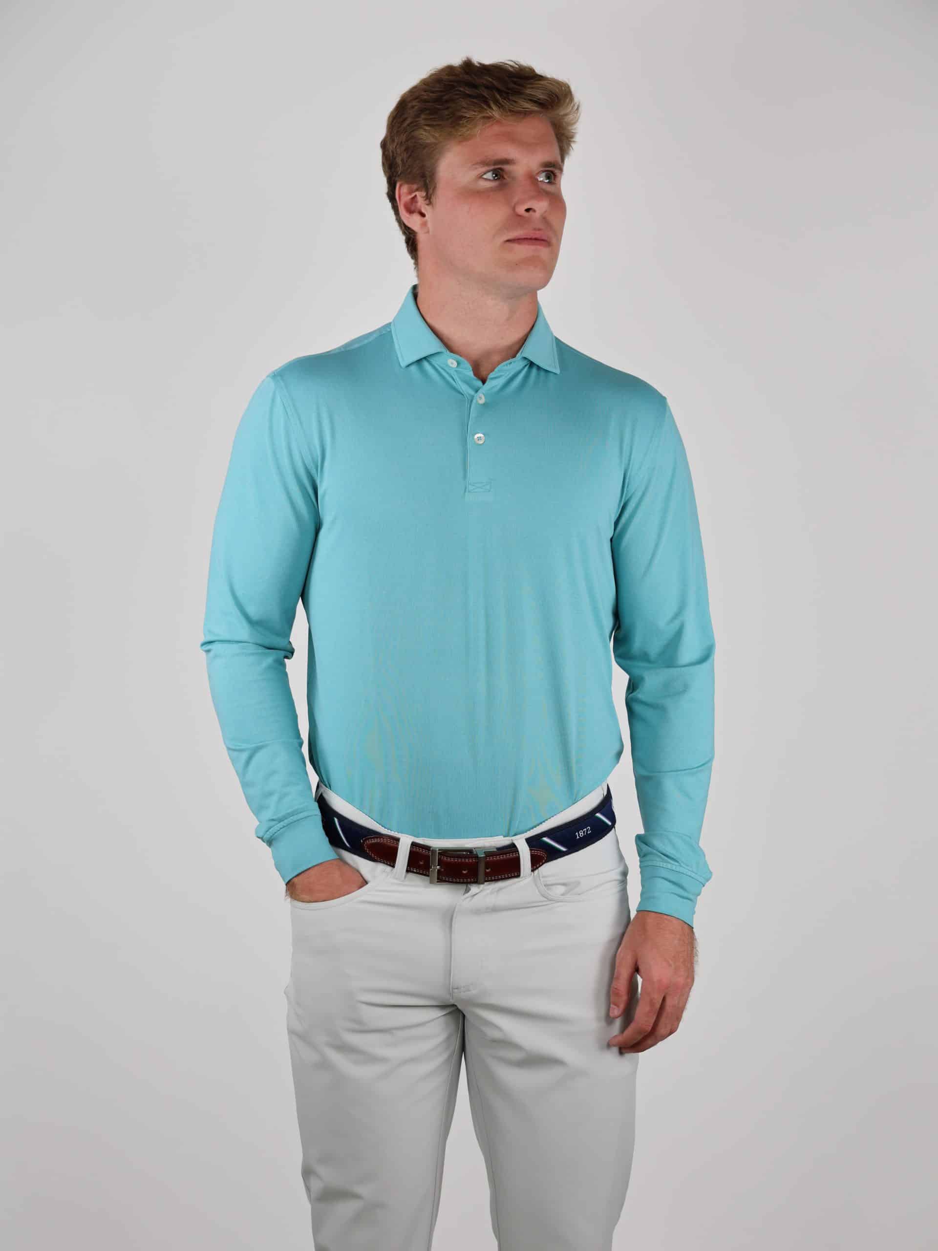 A person in a light blue long-sleeve polo and white pants stands against a plain background