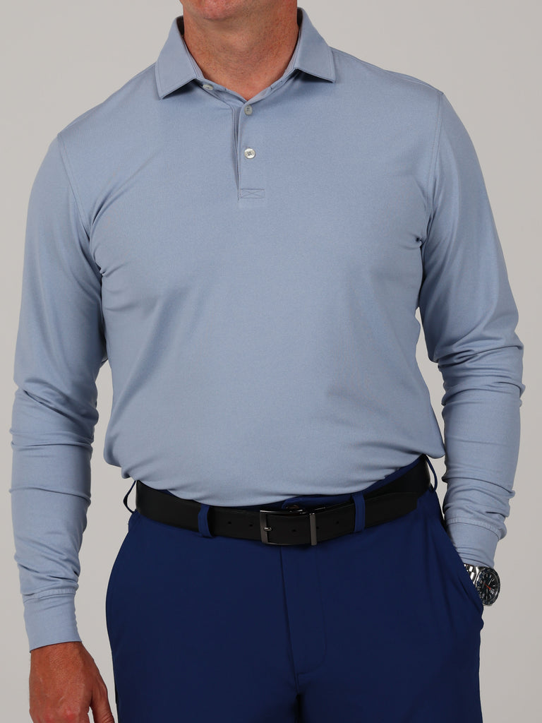 A person wearing a light blue long-sleeve polo shirt and navy pants is shown from the neck to knees. They have a black belt and a silver watch.
