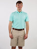 Smiling man wearing a light blue polo shirt and beige shorts, standing against a plain white background. He appears relaxed and content