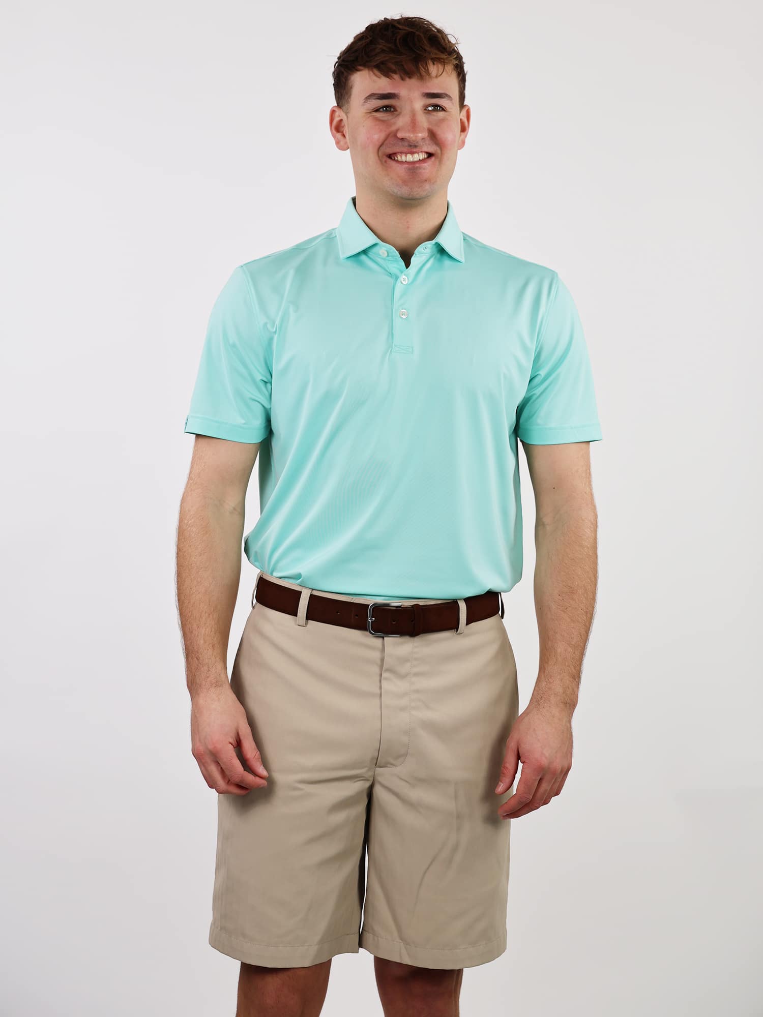 Smiling man wearing a light blue polo shirt and beige shorts, standing against a plain white background. He appears relaxed and content
