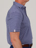 Man in a short-sleeve blue polo shirt with white stripes and a small logo on the sleeve cuff. He's wearing a brown belt, standing against a plain background.