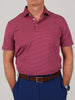 Man in a red and blue striped polo shirt with a buttoned collar, tucked into blue pants. He wears a brown belt and a watch, standing casually.