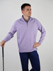 Man holding a golf club, wearing a light purple pullover and navy pants, stands confidently against a plain background