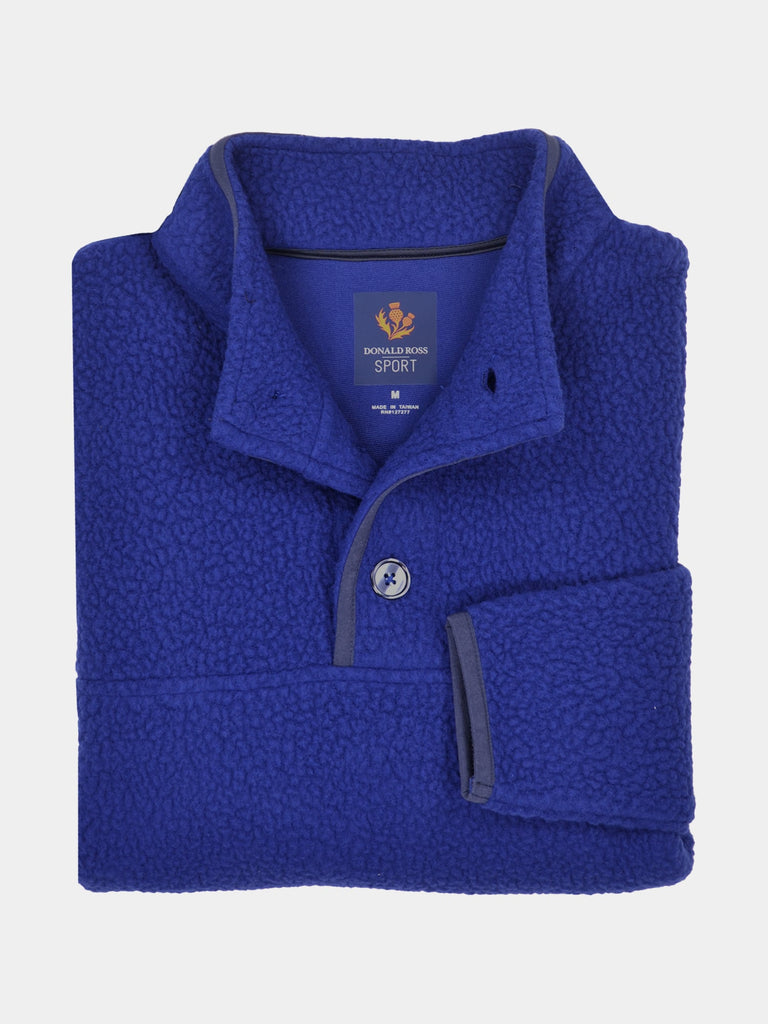 Folded royal blue fleece pullover with a high collar and button detail, featuring a label inside