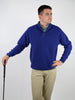 Man in a blue fleece sweater and beige pants holds a golf club, looking to the side with a thoughtful expression