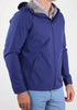 Man wearing a blue hooded jacket with a zipper over a patterned shirt. Paired with light blue pants, the outfit suggests a casual, stylish look.