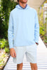 A man stands in a casual outfit featuring a light blue long-sleeve hoodie and striped shorts in a green outdoor setting.