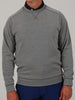 A person wearing a gray herringbone sweater and dark blue pants is standing with their arms at their sides against a neutral background.