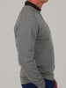 A person in a gray, long-sleeve shirt with thin stripes is viewed from the side against a neutral background. They wear blue pants, conveying a casual tone.
