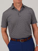 Man wearing a blue, yellow, and black striped polo shirt, brown belt, and blue pants. His left hand is in his pocket. Neutral gray background.