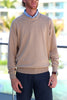 A man with a beard wears a tan sweater over a blue patterned shirt, standing outdoors with a blurred background.