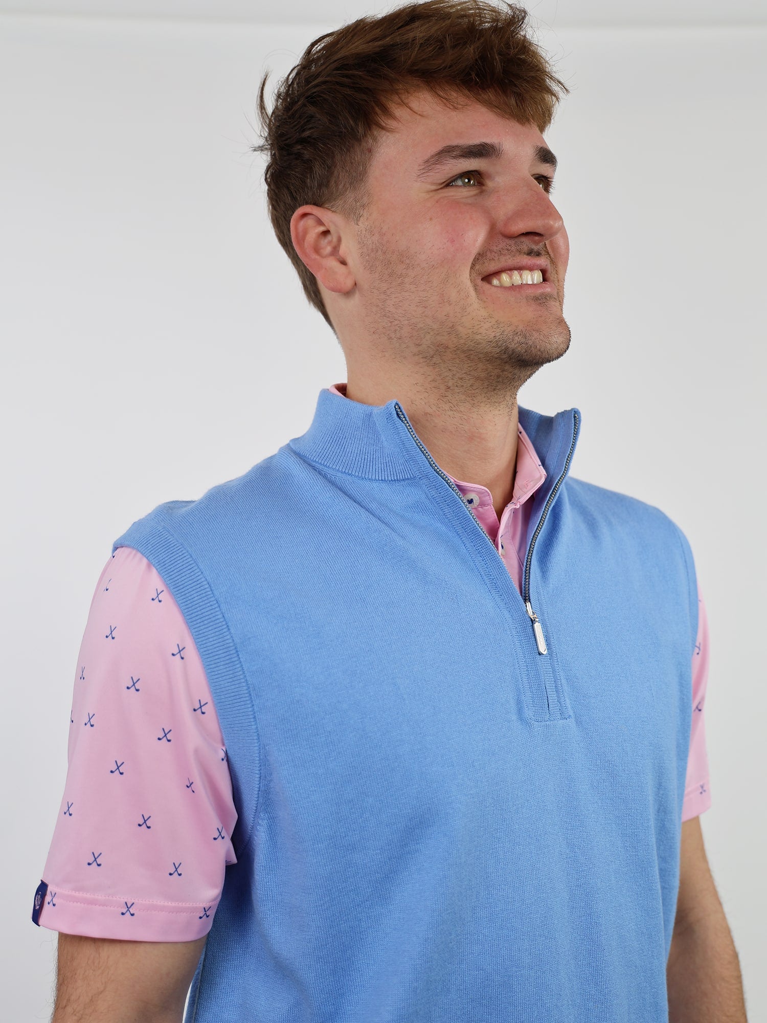 Smiling person in a blue sleeveless pullover over a pink shirt with small blue patterns