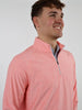A man smiling while wearing a coral quarter-zip pullover with a blue-striped shirt underneath