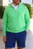A man is standing with his hands in the pockets of his navy shorts, wearing a bright green long-sleeve shirt with a zip collar.