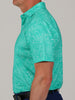 Side view of a man wearing a light turquoise short-sleeve shirt with a subtle floral pattern. He stands with a neutral expression against a plain background.