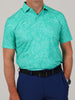 Man in a light teal floral polo shirt and dark blue pants with a black belt. His hand is in his pocket, conveying a casual, relaxed vibe.
