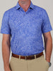 Man wearing a blue floral-patterned polo shirt with short sleeves, paired with beige pants and a brown belt. The tone is casual and stylish.