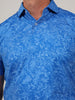 A close-up view of a person wearing a blue collared shirt with a detailed white floral pattern. The shirt conveys a casual, stylish tone.
