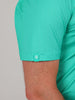 Close-up of a man's arm wearing a teal shirt with a subtle golf club and ball pattern. The sleeve has a small tag featuring a white emblem.