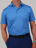 Man wearing a light blue polo shirt with subtle pattern, dark blue pants, and a black belt. His hands are in his pockets. The tone is casual.