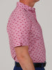 Side view of a person wearing a pink short-sleeve shirt with a small red shark pattern. The shirt is paired with navy pants.