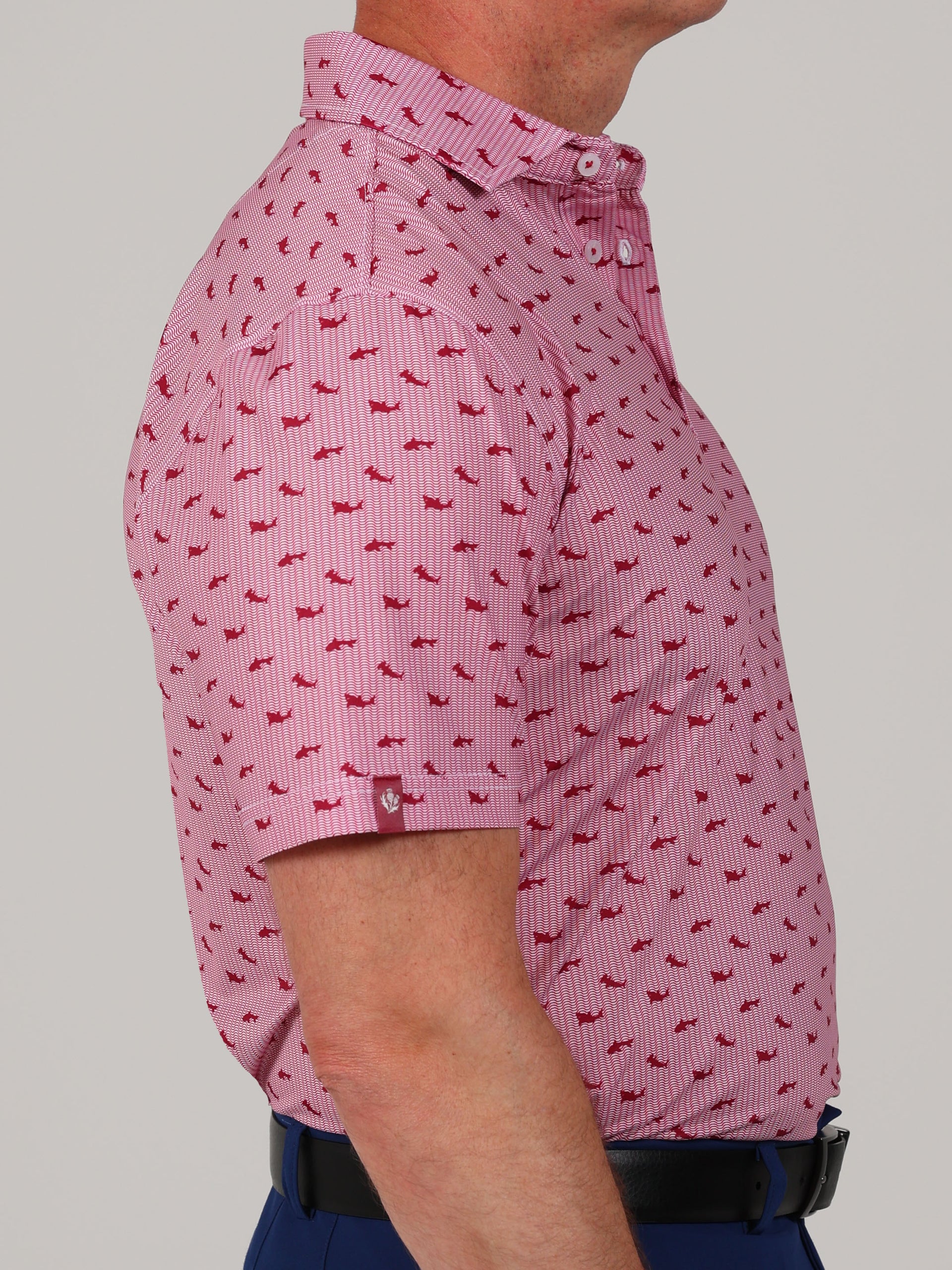Side view of a person wearing a pink short-sleeve shirt with a small red shark pattern. The shirt is paired with navy pants.