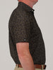 Side view of a person in a short-sleeve, football collage print polo shirt. They wear beige pants and a brown belt, against a plain background.