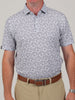 Man wearing a white short-sleeve shirt with a small, intricate football print pattern, paired with beige pants and a brown belt. The tone is casual and neat.