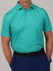 Man in turquoise polo shirt with abstract football pattern and navy pants, hands in pockets.