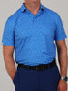 Man wearing a blue, football patterned short-sleeved shirt and dark blue pants with a black belt. He stands with one hand in his pocket, watch visible.