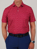 A man is wearing a red football patterned short-sleeve polo shirt with navy blue pants. He has a black belt and a silver watch.