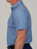 A man in a side profile wearing a blue, short-sleeve polo shirt with a camoflauge pattern. The background is plain gray, creating a neutral setting.